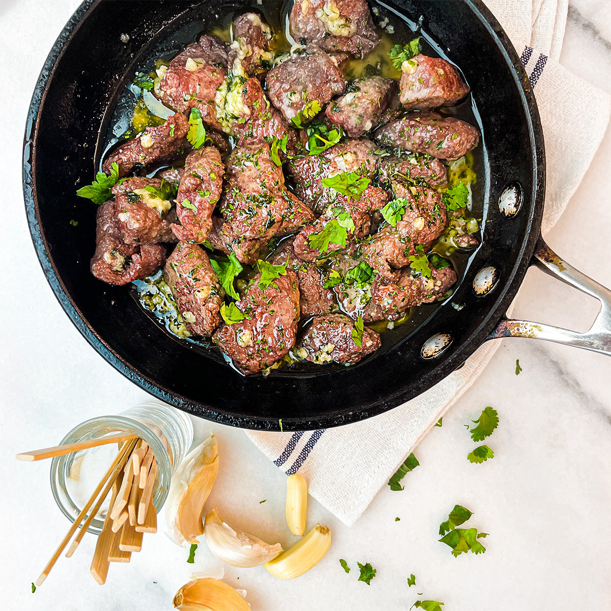 An overhead shot of a skillet filled with steak bites and butter and garlic and herbs.