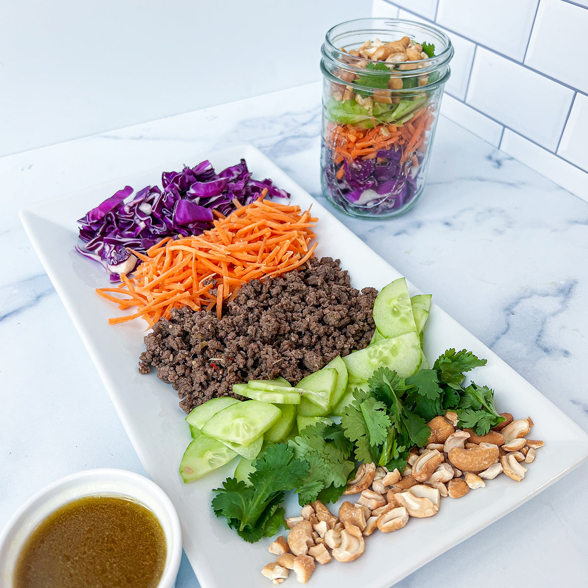 A platter and mason jar with layers of vegetables and meat