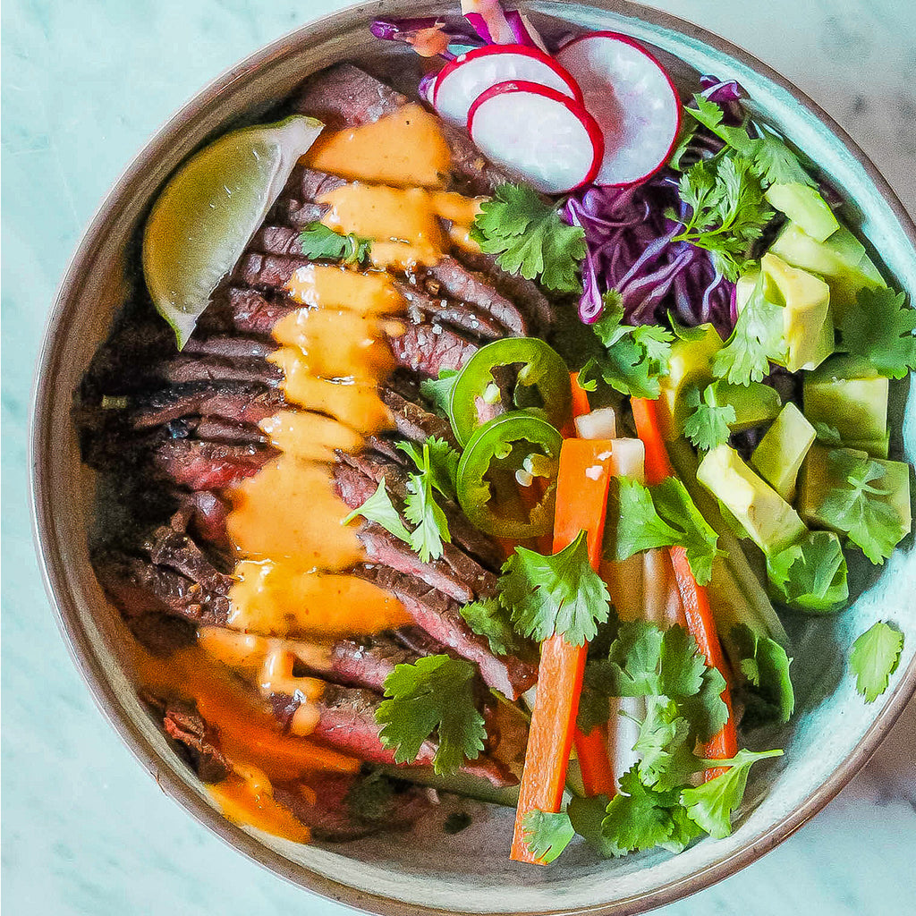 An overhead shot of sliced sirloin in a bowl with radishes, avocado, and pickles veggies