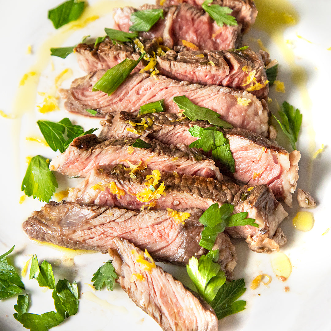 A bunch of slices of steak vertically down the center of the image topped with green herbs and lemon zest 
