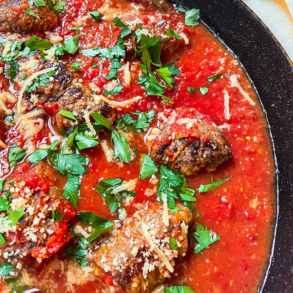 A skillet full of marinara and braciole rolls with parsley and parmasean cheese sprinkles.