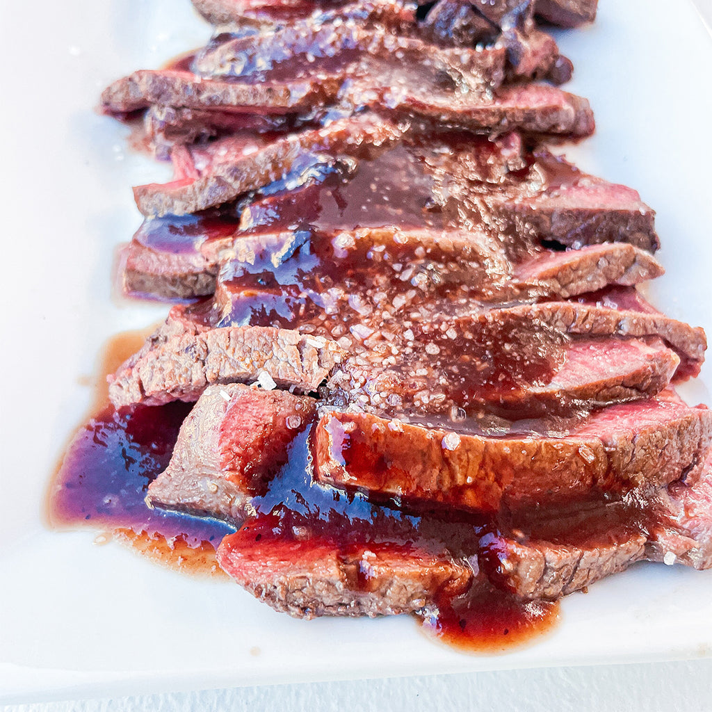 A white platter filled with slices of juicy steak and bordelaise sauce poured on top of the slices.