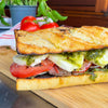 A footlong sandwich with tomatoes, basil, steak and mozzarella on a cutting board with tomatoes in the background.