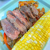 A camping plate with corn on the cob and filet mignon steak slices in between grilled peppers.