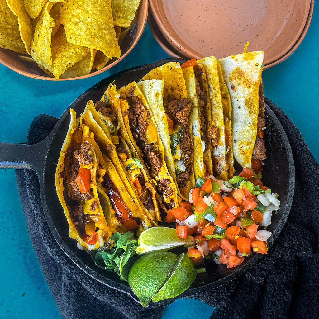 Quesadilla slices in a row inside a cast iron pan with limes and salsa and tortilla chips.